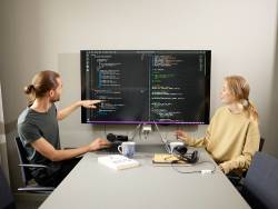 Två studenter sitter vid ett bord och diskuterar rader av kod som visas på en datorskärm.