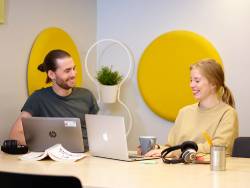 Två studenter sitter framför sina bärbara datorer och skrattar.